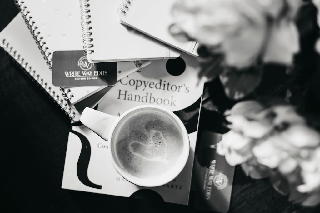 Flat lay image of a mug of coffee, editing books, notebooks, and Write Way Edits business cards.
